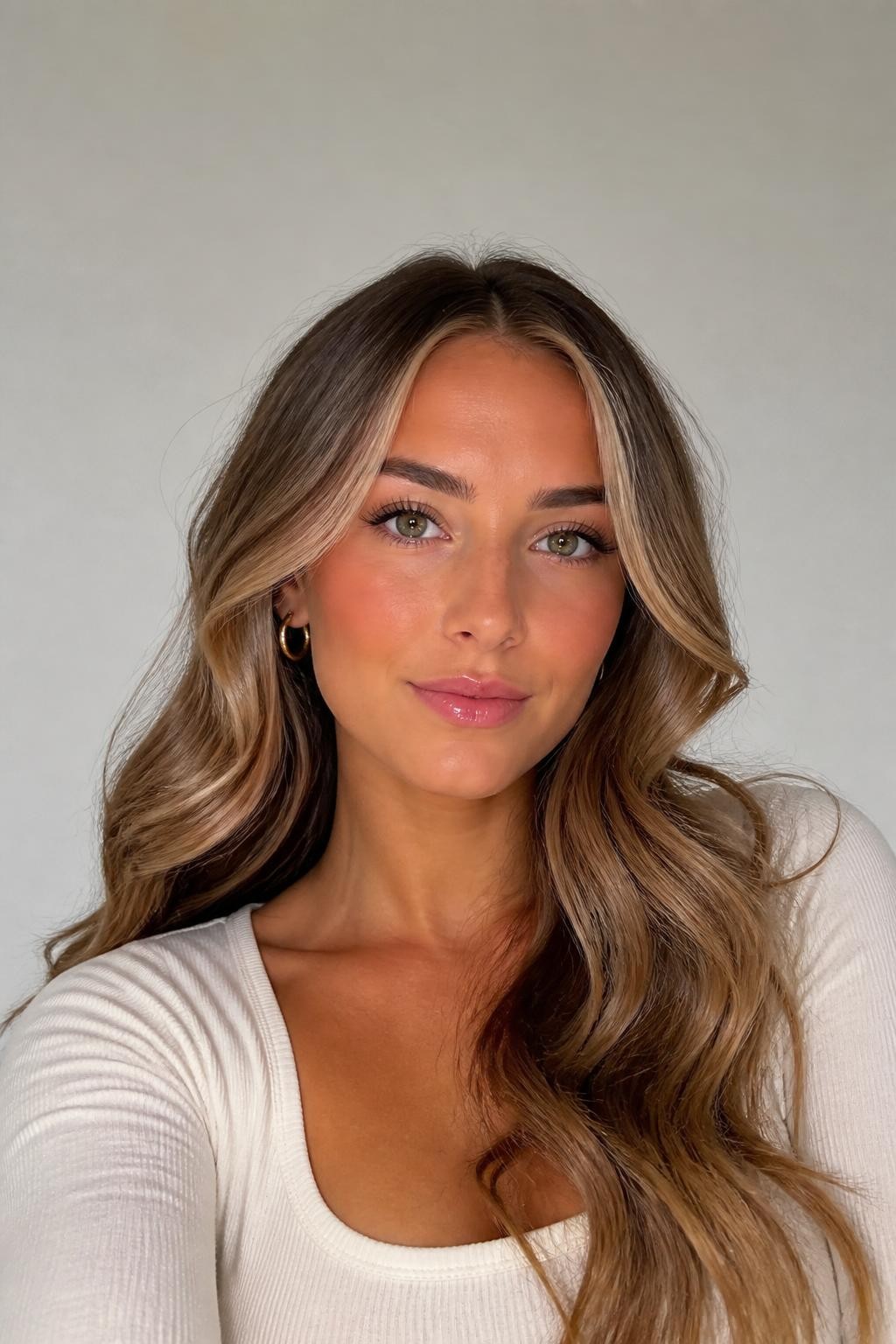 Image Prompt: A pretty woman with fair skin and light brown wavy hair with vanilla blonde money piece highlights, soft creamy blonde front sections framing the face, natural light brown base, loose waves with shine, fresh makeup, glossy lips, small gold hoops, fitted cream top, clean neutral studio background, close-up beauty portrait, realistic DSLR photo, clear face-framing blonde detail, no text, (no watermarks on images)