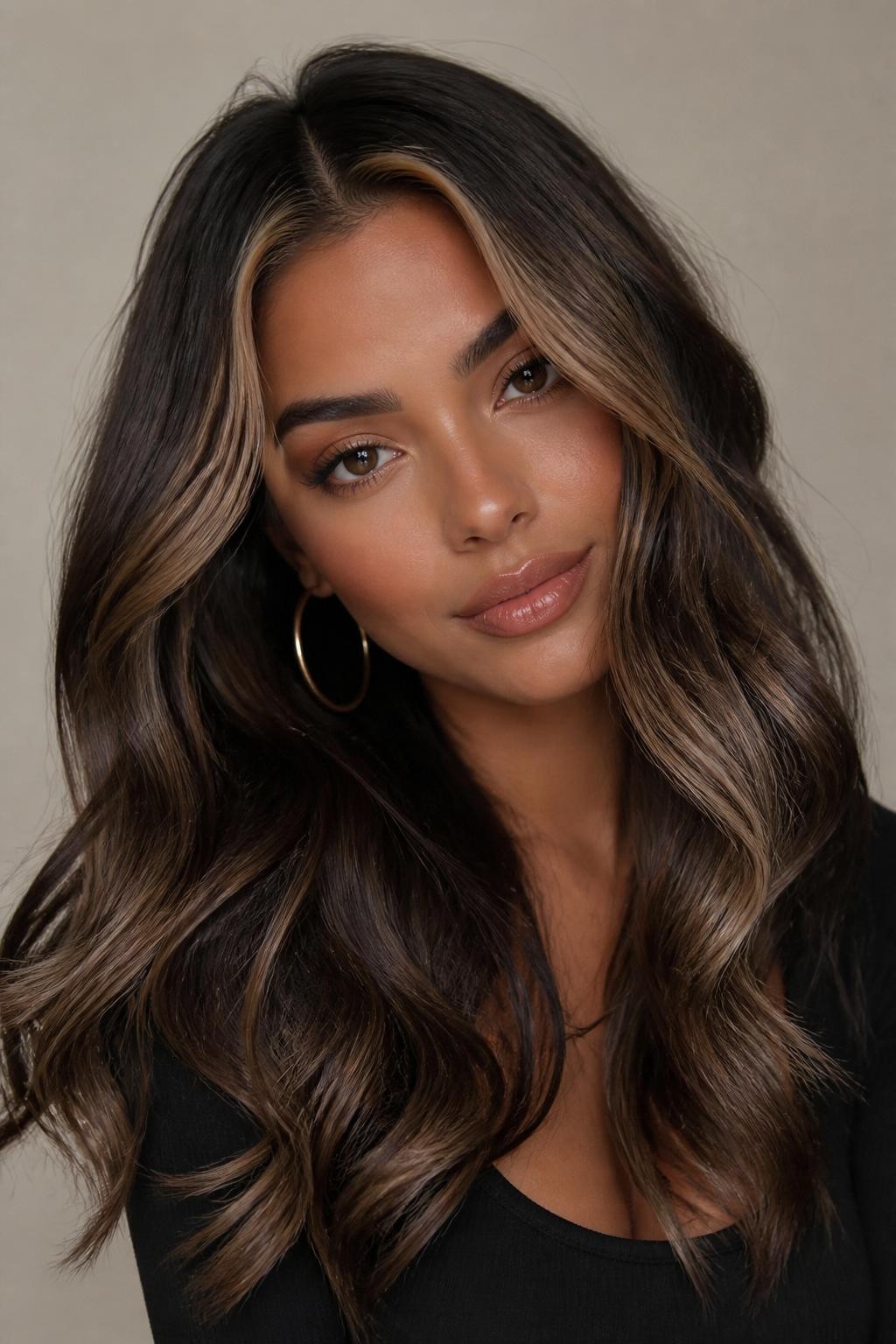 Image Prompt: A stylish woman with dark brunette wavy hair and milk brown money piece highlights, rich dark base with creamy milk brown front sections framing the face, loose waves with shine, warm medium-deep skin tone, glossy nude lips, subtle bronzed makeup, gold hoop earrings, fitted black top, clean neutral studio background, close-up beauty portrait, realistic DSLR photo, soft face-framing brunette color detail, no text, (no watermarks on images)