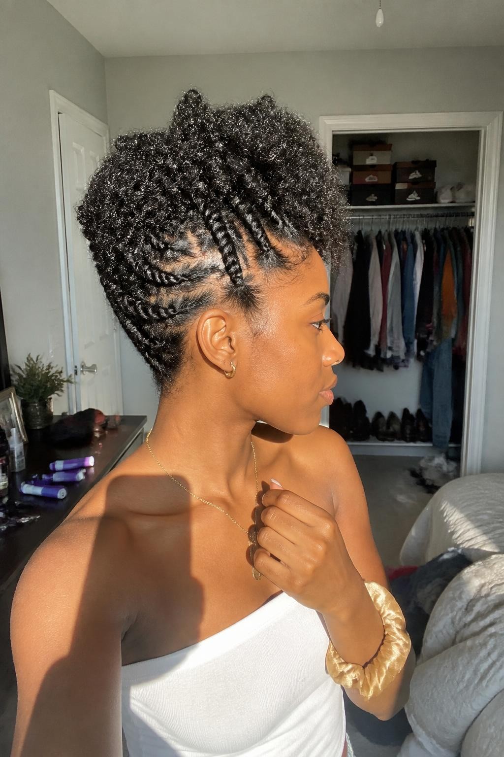Image prompt: Photo of a Black woman wearing upward flat twists with a full cluster of defined curls at the crown, side profile view, sun-drenched bedroom with a slightly open closet behind her, natural window light, containing perm rods on the dresser and a silk scrunchie around her wrist, realistic home styling moment, latest iPhone photo quality.
