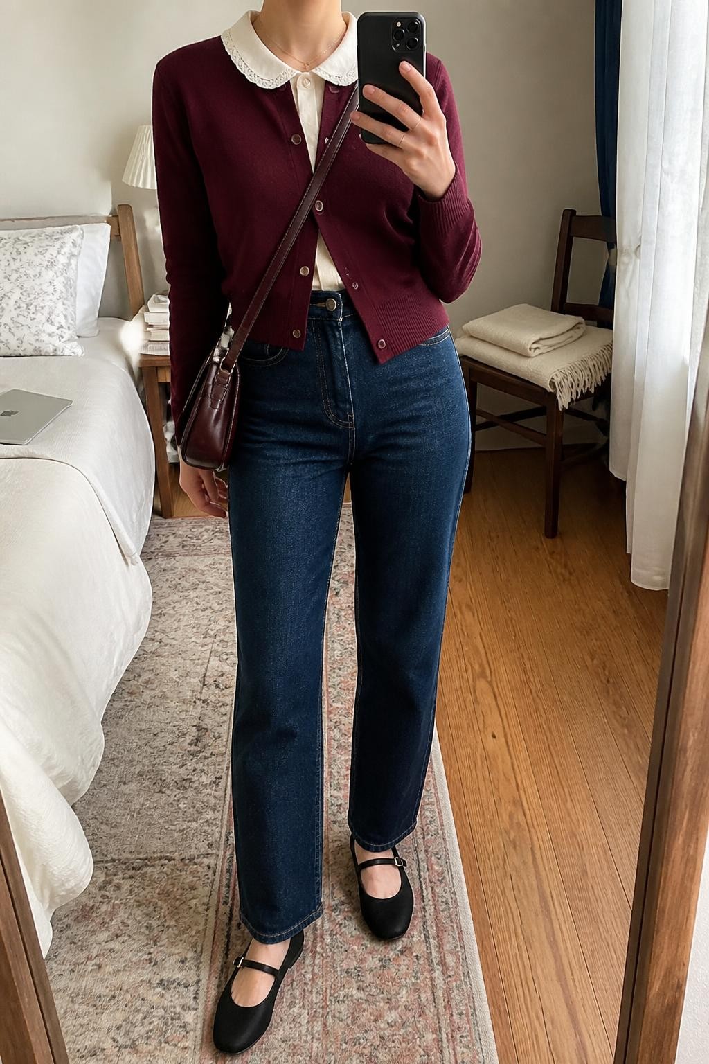 Image Prompt mirror selfie of a woman wearing a burgundy fine-knit V-neck cardigan partly buttoned over a cream cotton blouse with a lace-trimmed Peter Pan collar pulled over the cardigan neckline, dark-wash high-rise straight-leg jeans, black leather Mary Jane flats, and a burgundy leather crossbody bag, clearly showing the exact clothing items, colors, fabrics, collar, shoes, and bag listed in the Outfit Pieces section, holding a phone in front of a mirror, cropped at NECK so the face does not show, relaxed casual selfie pose in a cozy bedroom mirror setup, natural window light, with a folded blanket on a chair and a laptop on the bed, realistic knit, cotton, lace, denim, and leather textures, latest iPhone photo quality