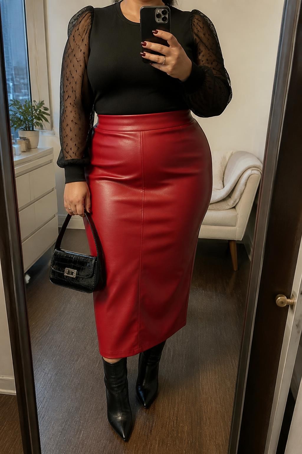 Mirror selfie of a plus size woman wearing a high-waisted red faux-leather midi skirt with a straight silhouette, a fitted black top with sheer dotted long sleeves and an opaque bodice, black pointed ankle boots, and a small black patent handbag, clearly showing the exact outfit pieces, red leather texture, sheer sleeve details, colors, footwear, and accessories listed, holding a phone in front of a mirror, cropped at the neck so the face does not show, relaxed confident selfie pose, in a stylish city apartment with soft indoor lighting, a small plant on a dresser and a folded blanket on a chair, realistic bold Christmas dinner appearance, latest iPhone photo quality.