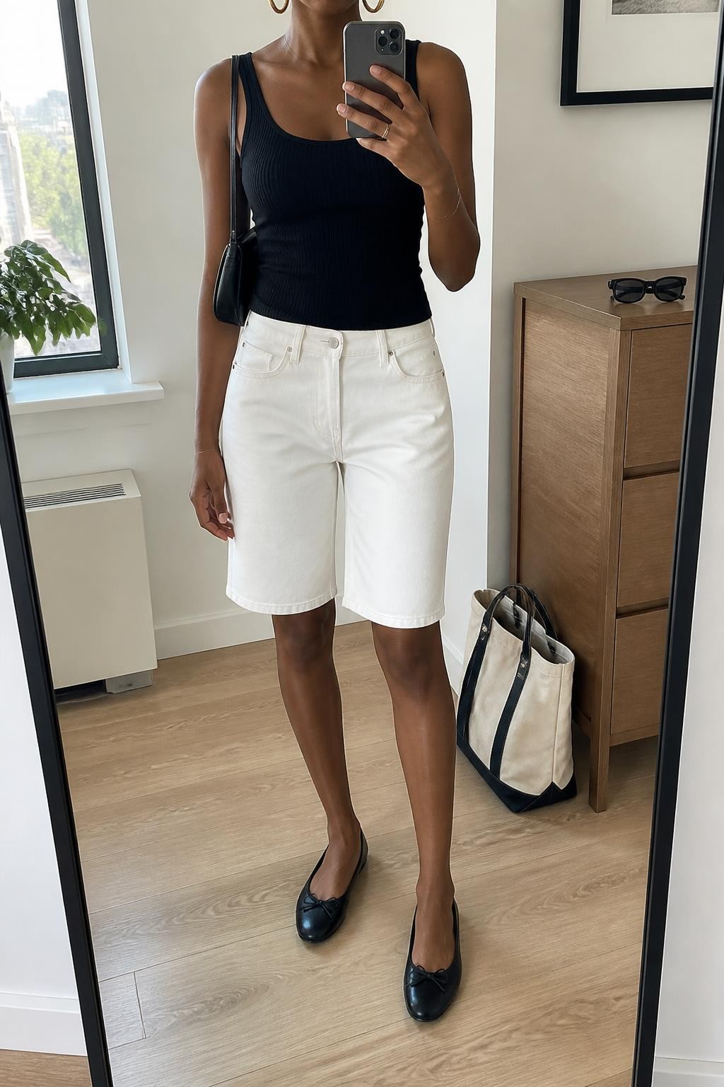 mirror selfie of a Black woman wearing clean white straight-cut denim jorts with a relaxed knee-length fit, a fitted black ribbed cotton tank top, black leather ballet flats, a compact black leather shoulder bag and medium gold hoop earrings, wearing exactly the listed clothing and accessories with no additional garments, holding a phone in front of a mirror, cropped at NECK so the face does not show, relaxed casual selfie pose, in a stylish city apartment, natural window light, sunglasses placed on a dresser and a tote bag resting on the floor, realistic denim texture and natural proportions, latest iPhone photo quality.